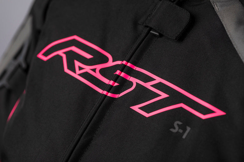 Detaljerad vy av RST-logotypen på framsidan av RST Dam Textil Mc-Jacka S-1 Mesh Svart/Rosa med tydlig S-1 märkning.