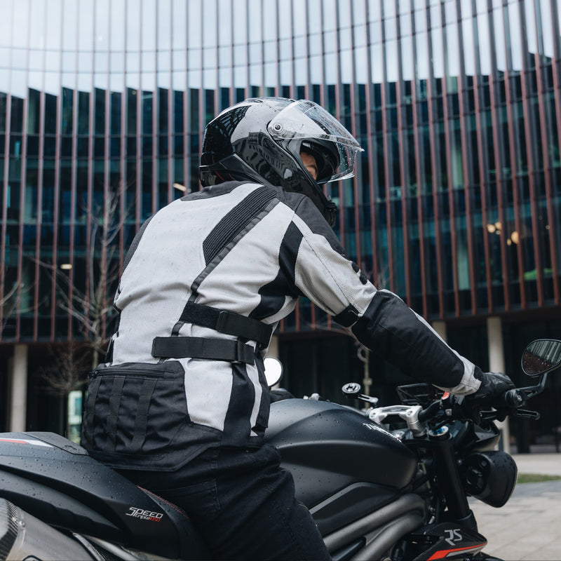 Motorcyklist som bär Rebelhorn Textil Mc-Jacka Scandal Grå, fotograferad bakifrån på en motorcykel i stadsmiljö.